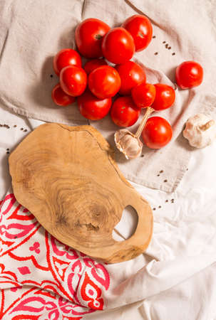 Cutting board made of olive tree, next to a bunch of tomatoes, garlic, pepper. View from above of fresh vegetables, lying on a tablecloth, for cooking healthy dishes.の写真素材