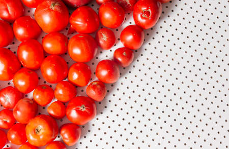Ripe tomatoes lie on a white table with round holes. Top view. The background is divided diagonally, there is an empty space for text, menus, recipes.の写真素材