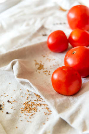 Red tomatoes on a linen towel. In the folds of the fabric of the moaning pepper and mustard in the grains. Ripe vegetables for dietary menus, recipes for healthy and healthy food. Vertical photo.の写真素材