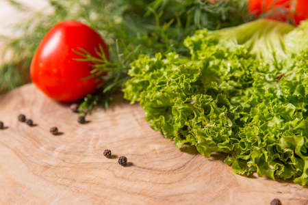 Fragment of cutting board made of olive tree, on which lie lettuce, dill, tomatoes. Pepper is scattered on the tablecloth. Ingredients for a salad of fresh vegetables.の写真素材