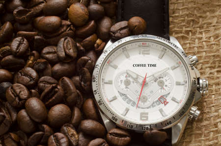 Silver watch with black leather belt and coffee beans on canvasの写真素材