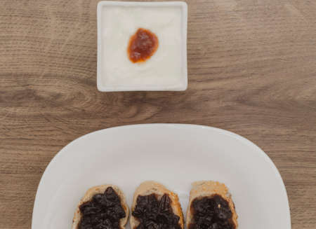 Jam on slices of bread and yogurt in white bowl on wood backgroundの写真素材