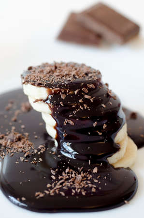 Slices of banana with poured chocolate and chocolate bars on white backgroundの写真素材