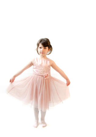 Sweet toddler girl in beautiful pink dress make gymnastics on whiteの写真素材