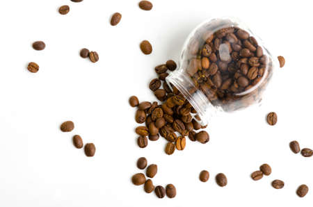 Jar with coffee beans spilling out on white backgroundの写真素材