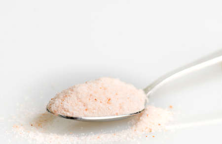 Rose salt crystals in steel spoon isolated on white background