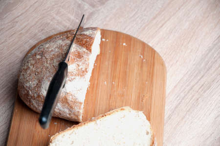 Cutting board, bread and a knife lying on a wooden tableの写真素材