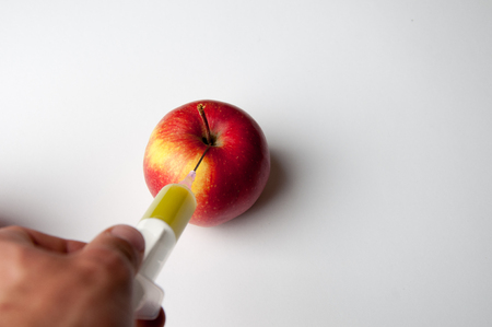 Red apple with a hypodermic needle/syringe in it isolate on whiteの写真素材