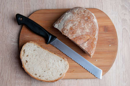 Cutting board, bread and a knife lying on a wooden tableの写真素材