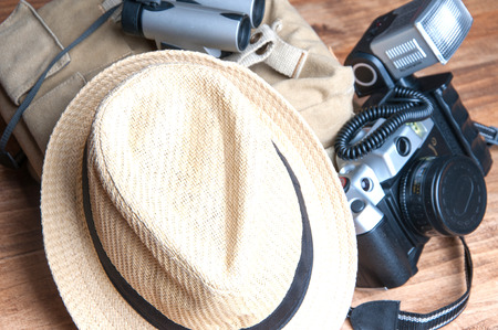 Tourism concept. Backpack, hat , binocular and old camera isolated on wooden background.の写真素材