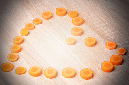 On a wooden table laid out pieces of carrot in the form of heart.の写真素材