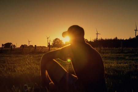The man sitting in a meadow at sunset. Windmills in the background.の写真素材