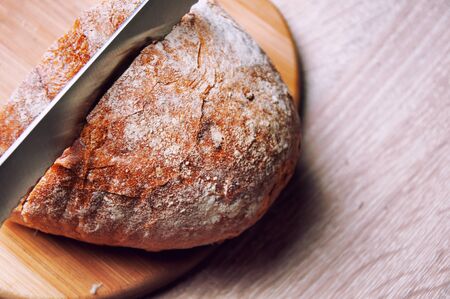 Cutting board, bread and a knife lying on a wooden tableの写真素材