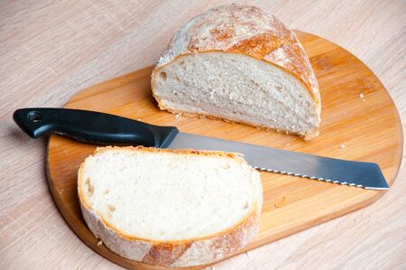Cutting board, bread and a knife lying on a wooden table
