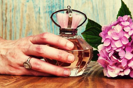 Hand holding a perfume and hydrangea wooden backgroundの写真素材