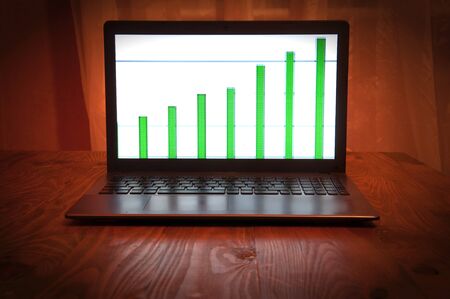 Laptop with business graph placed on wooden desktop.の写真素材