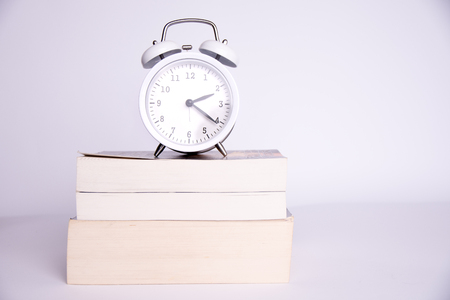 clock standing on the books on a white background.の写真素材