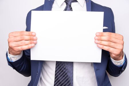 man in a blue suit holding a white card. Place for text.の写真素材