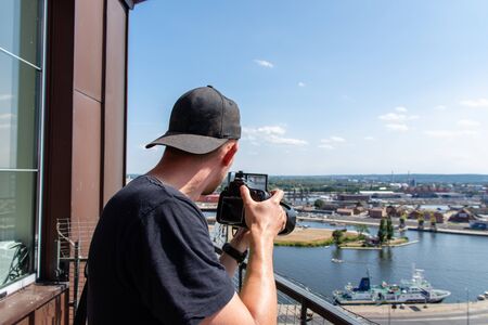 Young male photographer taking pictures with professional camera from a balcony with great cityscape view of ancient Varanasi ghats background. Varanasi, India, circa march 2017の写真素材