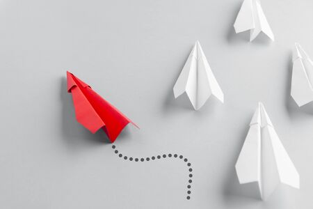 Red paper plane as a leader. White planes follow him. White background.