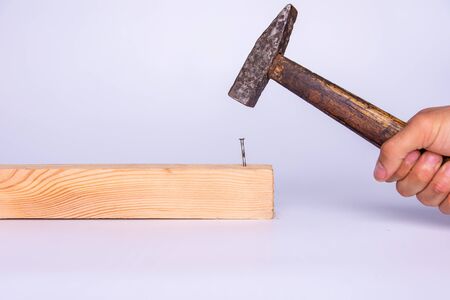 A hand holding a hammer and hammering a nail. White background.の写真素材