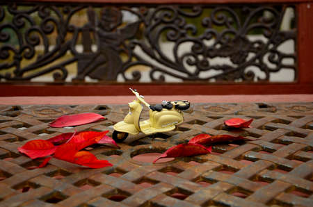 Small yellow scooter toy on the metal garden chair and table with red leafs in autumnの写真素材
