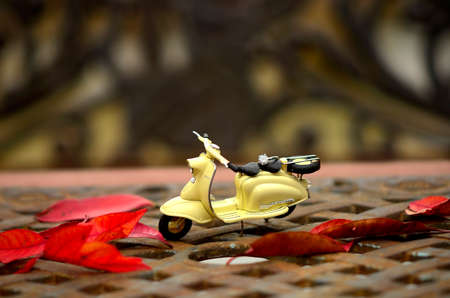 Small yellow scooter toy on the metal garden chair and table with red leafs in autumnの写真素材