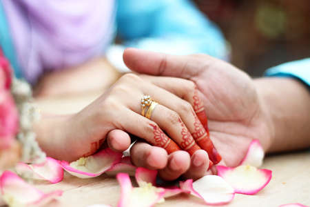 malay wedding groom bolstering gold ring on bride's fingerの写真素材