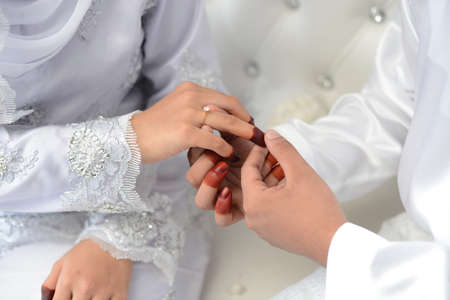 malay wedding groom bolstering gold ring on bride's fingerの写真素材
