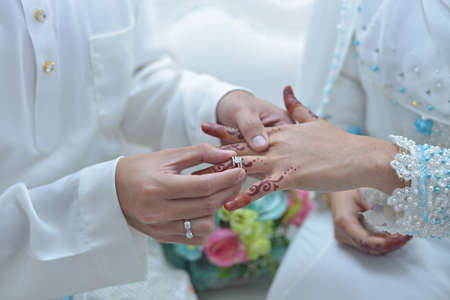 malay wedding groom bolstering gold ring on bride's fingerの写真素材