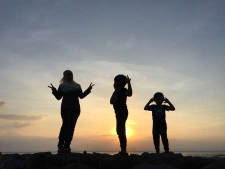 silhouette of two sibling with young mother playing on sunset backgroundのeditorial素材