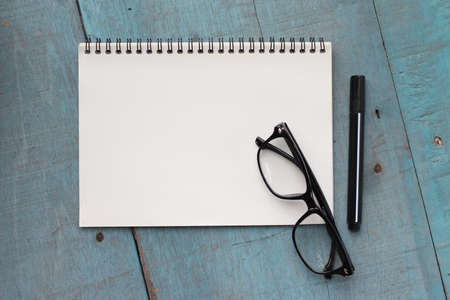 Top view of office desk table with open spiral notebook, pencil, and small tree in a white pot on wood tableの写真素材