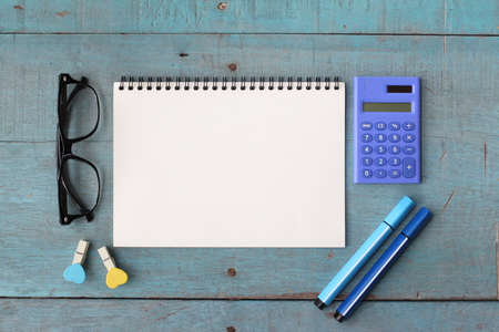 Top view of office desk table with open spiral notebook, pencil, and small tree in a white pot on wood tableの写真素材