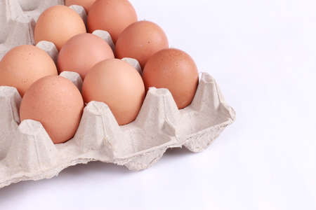 Close-up view of raw chicken eggs in egg box on white wooden background
