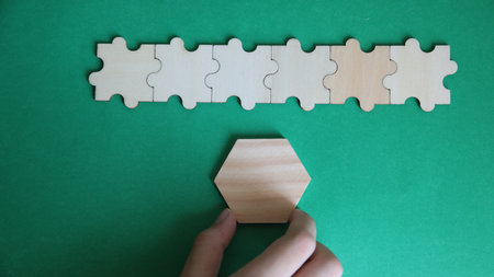 Hands of a man assembling jigsaw puzzle on green background.の写真素材