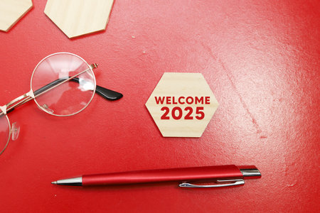 WELCOME 2025 wooden block with pen and glasses on red backgroundの写真素材