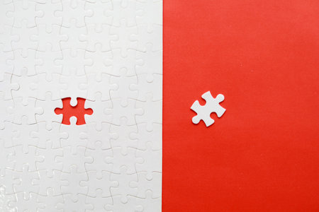 Top view of white jigsaw puzzle with missing piece on red and white background