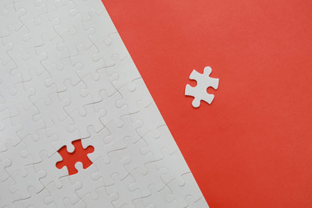 Top view of white jigsaw puzzle with missing piece on red and white background