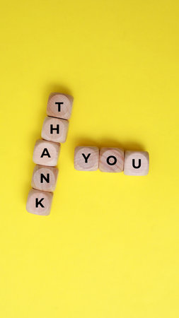 Thank you on wooden cubes on a yellow background. Copy space.