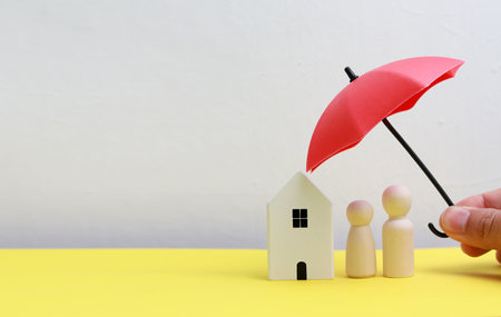 Insurance concept with house and people figures and red umbrella on yellow tableの写真素材