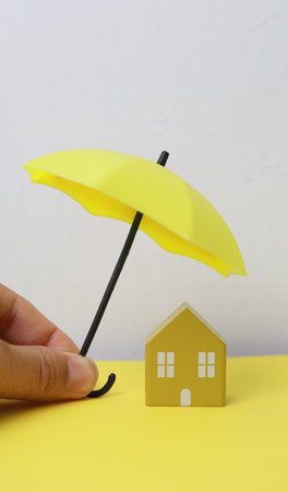 Paper house and yellow umbrella on yellow and white background, insurance conceptの写真素材
