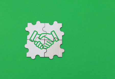 Jigsaw puzzle with handshake icon on green background. Business concept.の写真素材