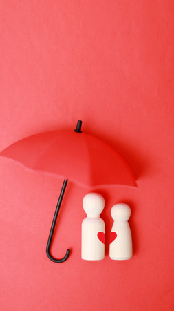 two wooden figures under an umbrella on a red background. insurance conceptの写真素材