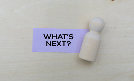 What's next? Text on sticky note with wooden doll on wooden backgroundの写真素材