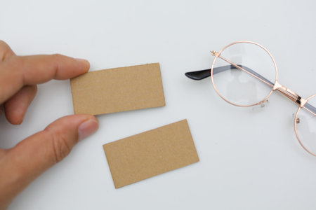 Hand holding blank business card and eyeglasses on white background.