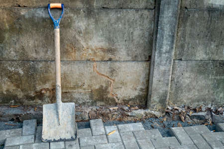 an old hoe leaning against a wall, placed on a paving block, photographed in the daytimeの写真素材
