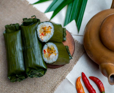 Arem-arem. Indonesian traditional food made from rice filled with spicy stir-fried carrot chicken wrapped in banana leaves, photographed with chiliの写真素材