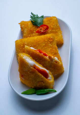 Risol pieces on a white plate, decorated with green chilies