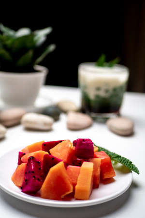 Slices of papaya and dragon fruit on a white plate with ice cendol background photographed on a...