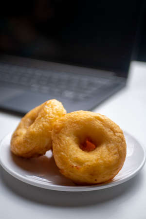 Brown Doughnut Potatoes, with blurry laptop as background, photographed on white plate and white tableの写真素材